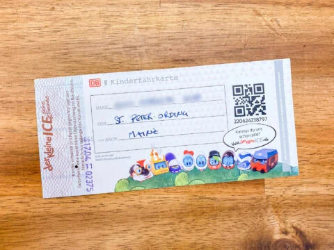 Kinderfahrkarte der Deutschen Bahn mit handschriftlicher Eintragung von St. Peter-Ording nach Mainz auf einem Holztisch.