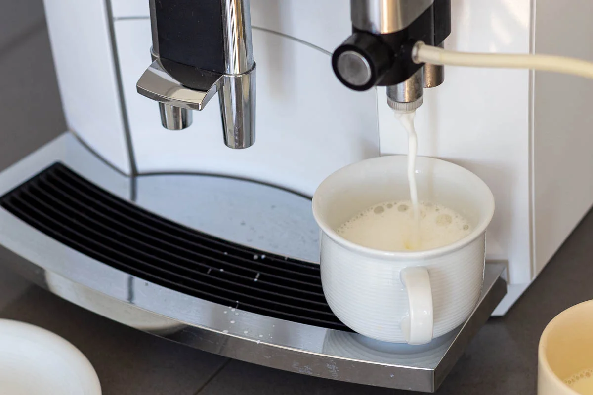 Eine Kaffeemaschine füllt Milch in eine weiße Tasse auf der Abtropffläche.