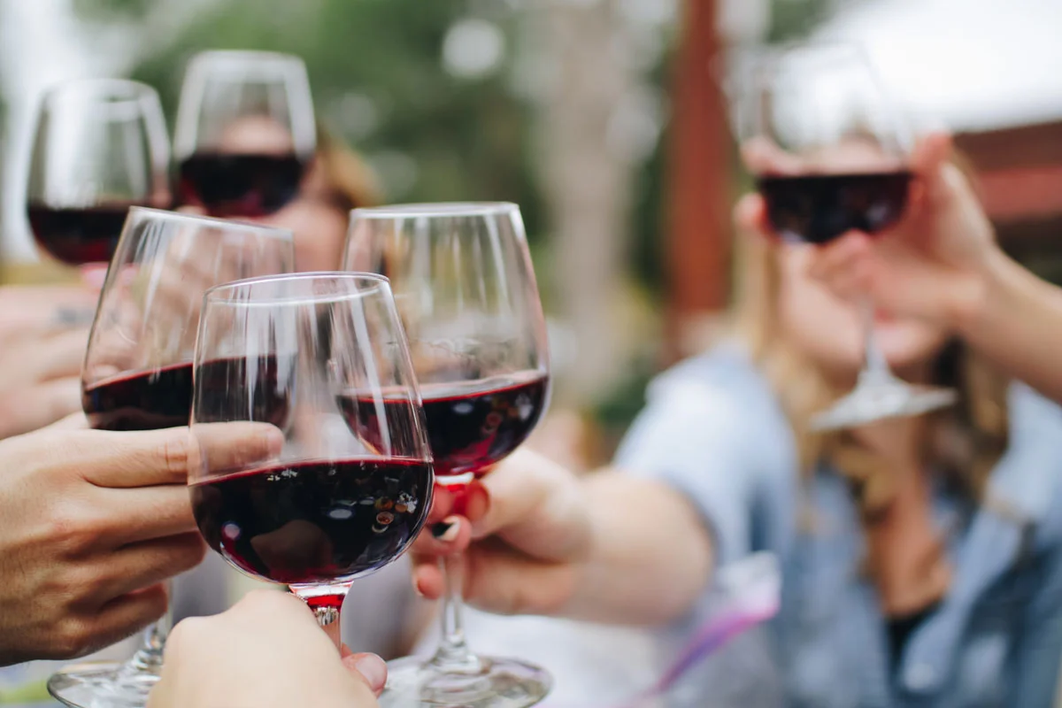 Mehrere Personen stoßen mit Gläsern Rotwein im Freien an.