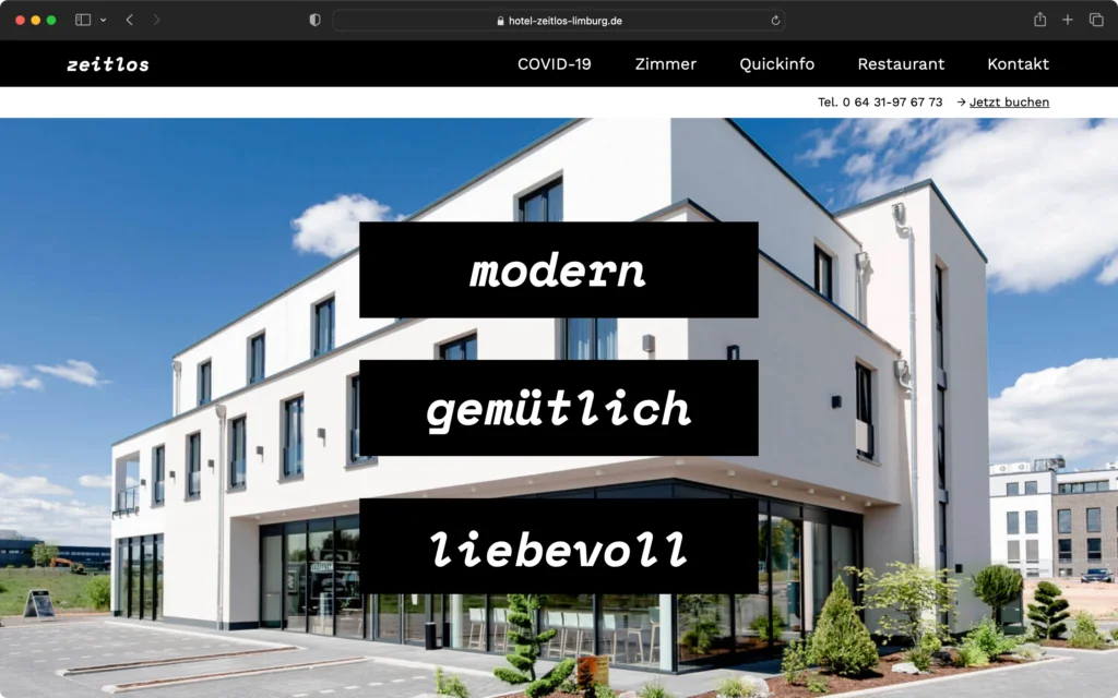 Außenansicht eines modernen, weißen mehrstöckigen Gebäudes mit großen Fenstern und gepflastertem Vorplatz unter blauem Himmel.
