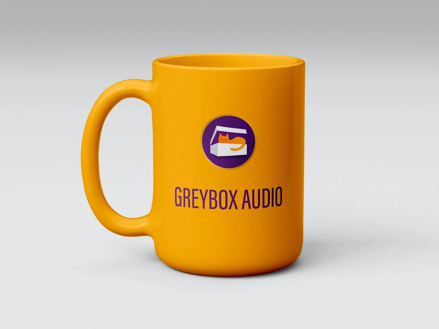Gelbe Tasse mit einem Logo einer orangefarbenen Katze in einer weißen Box und dem Text Greybox Audio auf grauem Hintergrund.