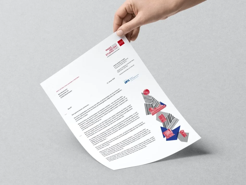 Hand hält ein Blatt Papier mit gedrucktem Text und farbigen grafischen Elementen auf grauem Hintergrund.