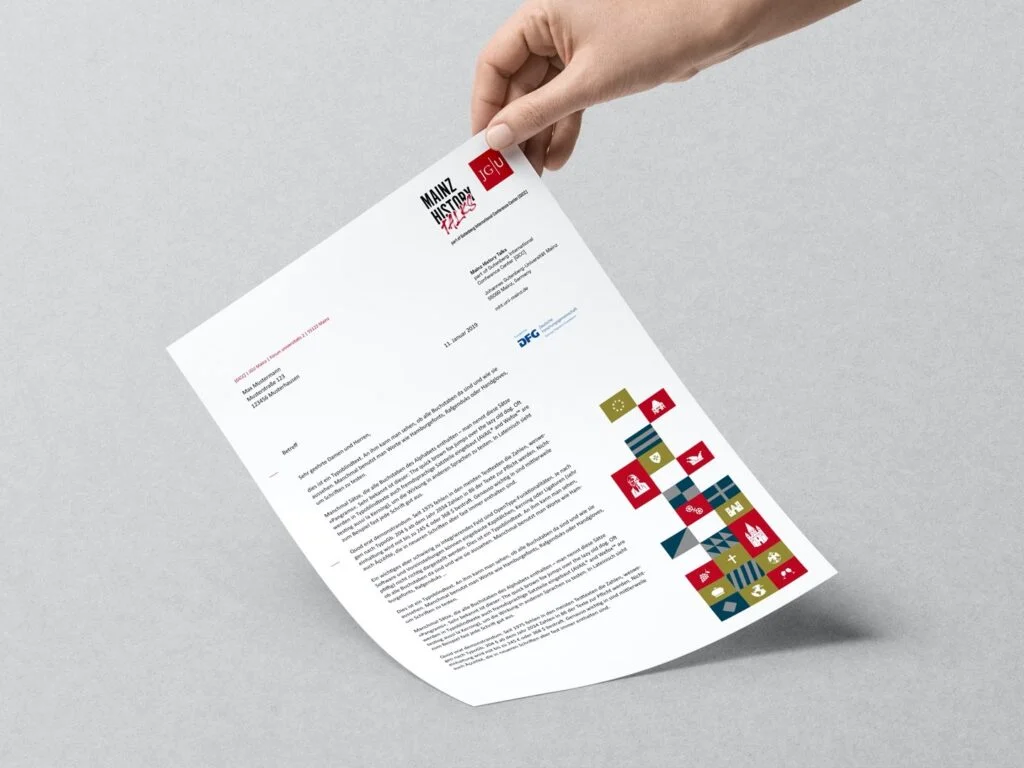 Hand hält ein Blatt Papier mit Text und buntem Logo auf grauem Hintergrund.