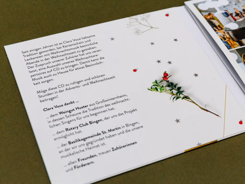 Aufgeklappte Broschüre mit Text in deutscher Sprache, Sternen und einem Zweig mit roten Beeren auf weißem Hintergrund.