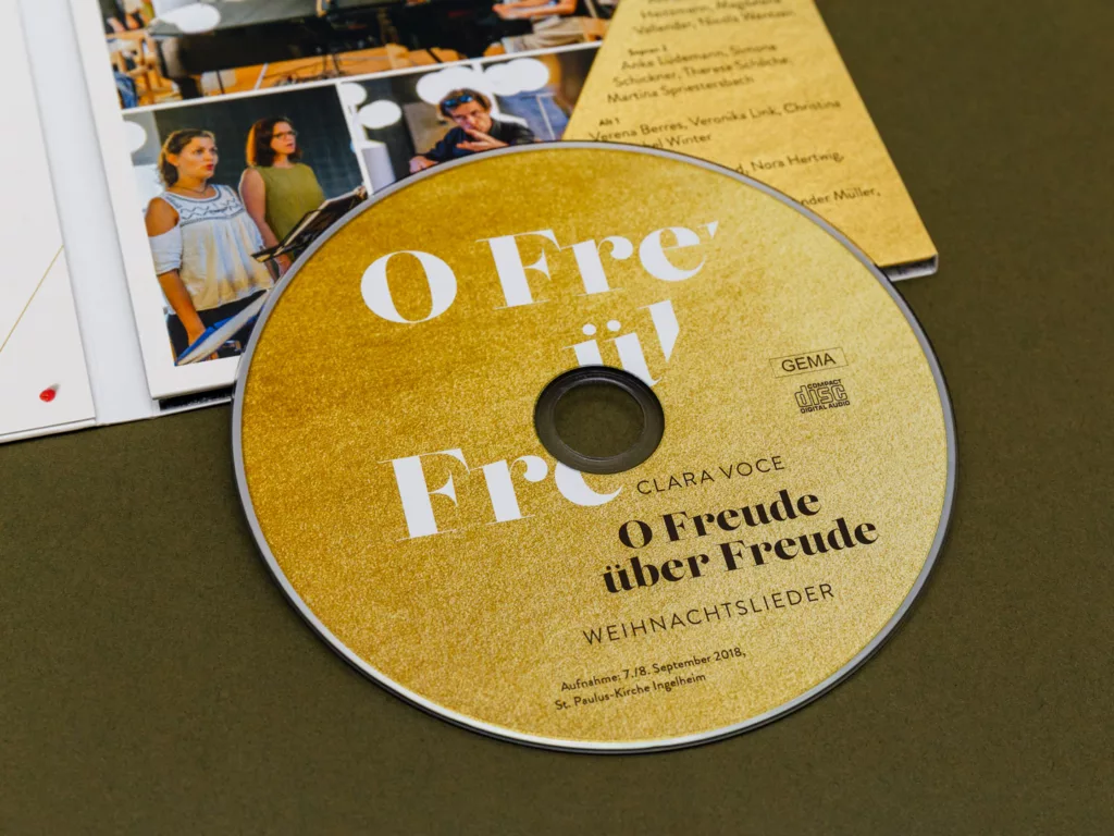 CD mit goldfarbenem Etikett und der Aufschrift O Freude über Freude Weihnachtslieder, daneben ein aufgeklapptes Booklet mit Fotos und Text.