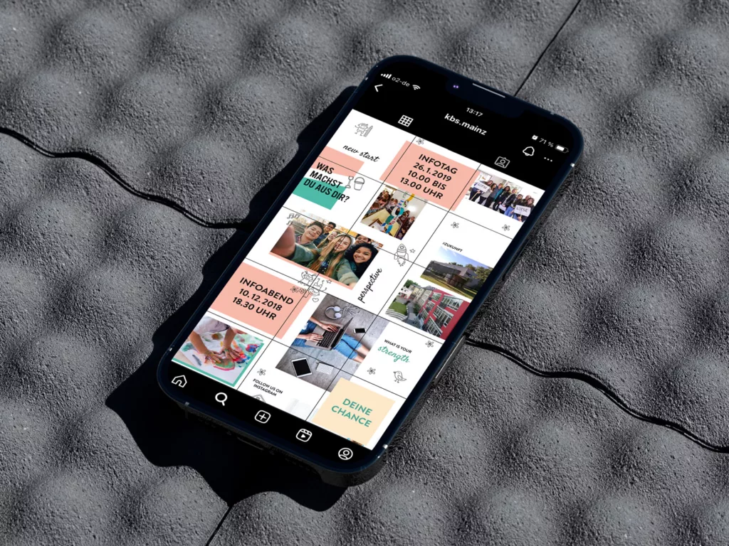 Smartphone liegt auf einer grauen, strukturierten Oberfläche und zeigt ein Instagram-Profil mit mehreren Beiträgen und Texten in deutscher Sprache.