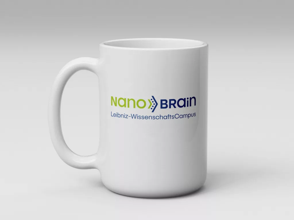Weiße Tasse mit dem Schriftzug NanoBrain Leibniz-WissenschaftsCampus in grüner und blauer Schrift auf weißem Hintergrund.