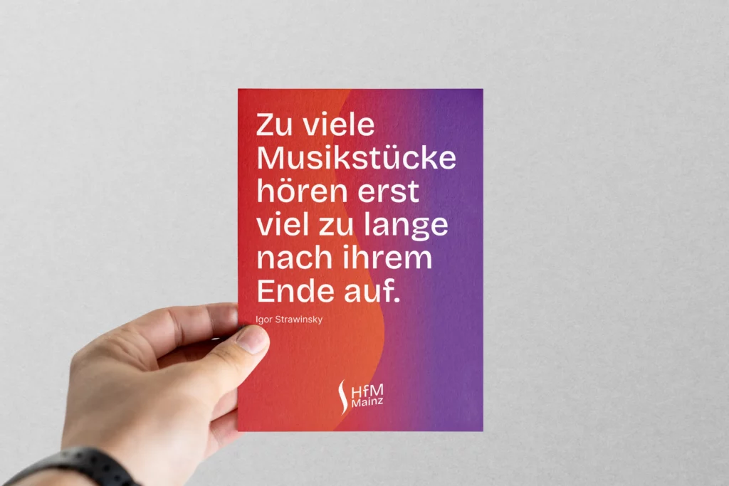 Hand hält eine Karte mit Farbverlauf von Rot zu Lila und weißem Text eines Zitats von Igor Strawinsky.